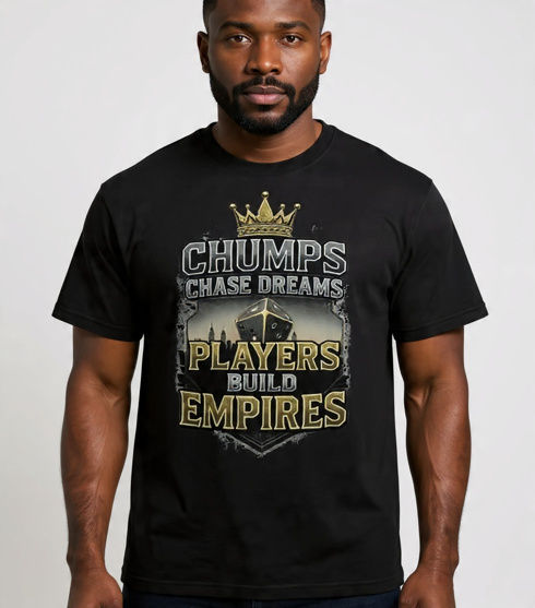 A professional fashion mockup of a black heavyweight garment-dyed t-shirt. The chest graphic features a large shield design with a golden crown on top and a metallic die in the center, emblazoned with the bold text "CHUMPS CHASE DREAMS. PLAYERS BUILD EMPIRES. 1